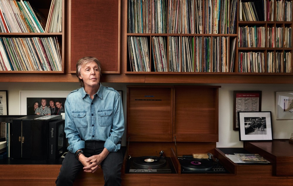 Paul McCartney sitting next to a turntable and in front of a vinyl record collection